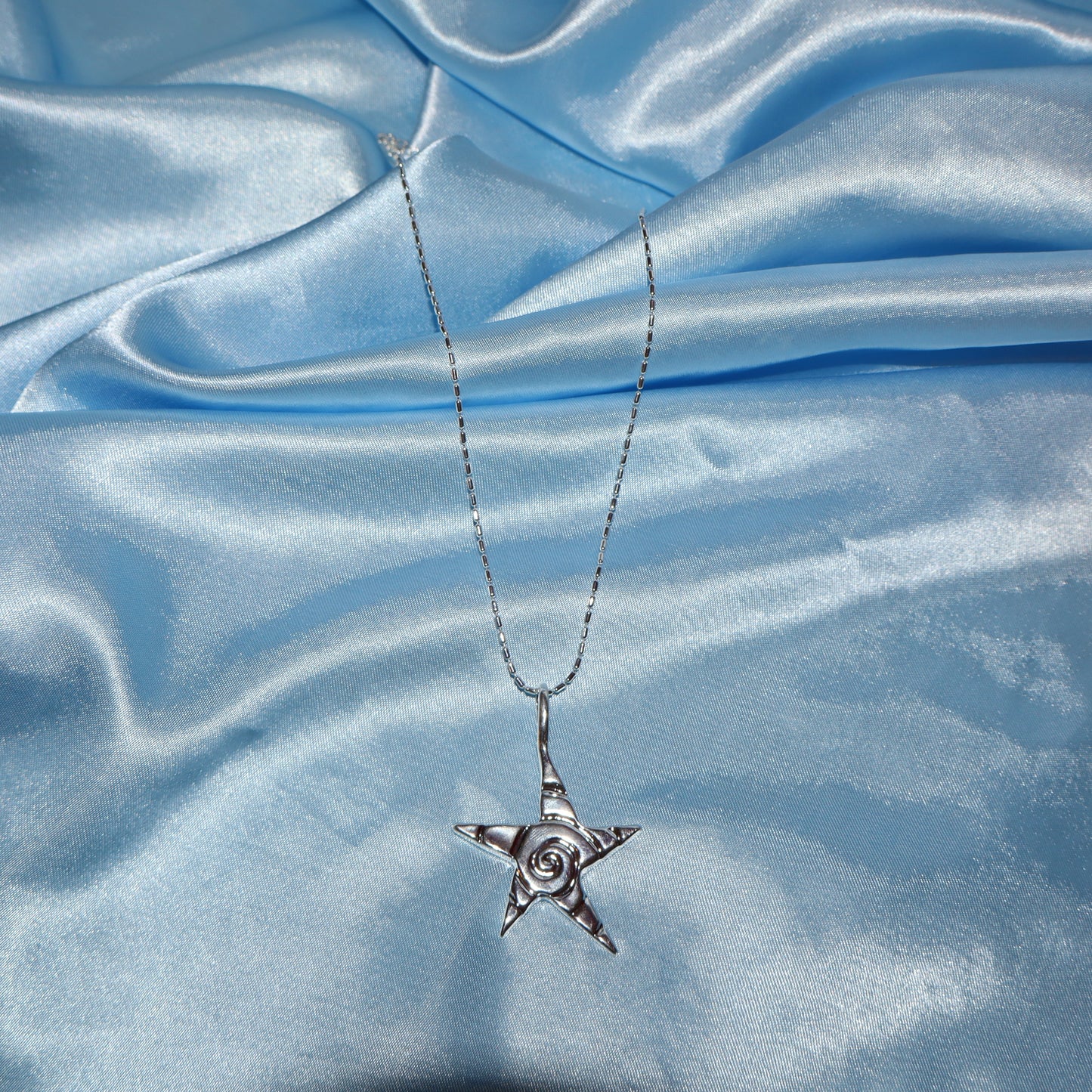 Star pendant, with a swirl design, silver chain necklace.