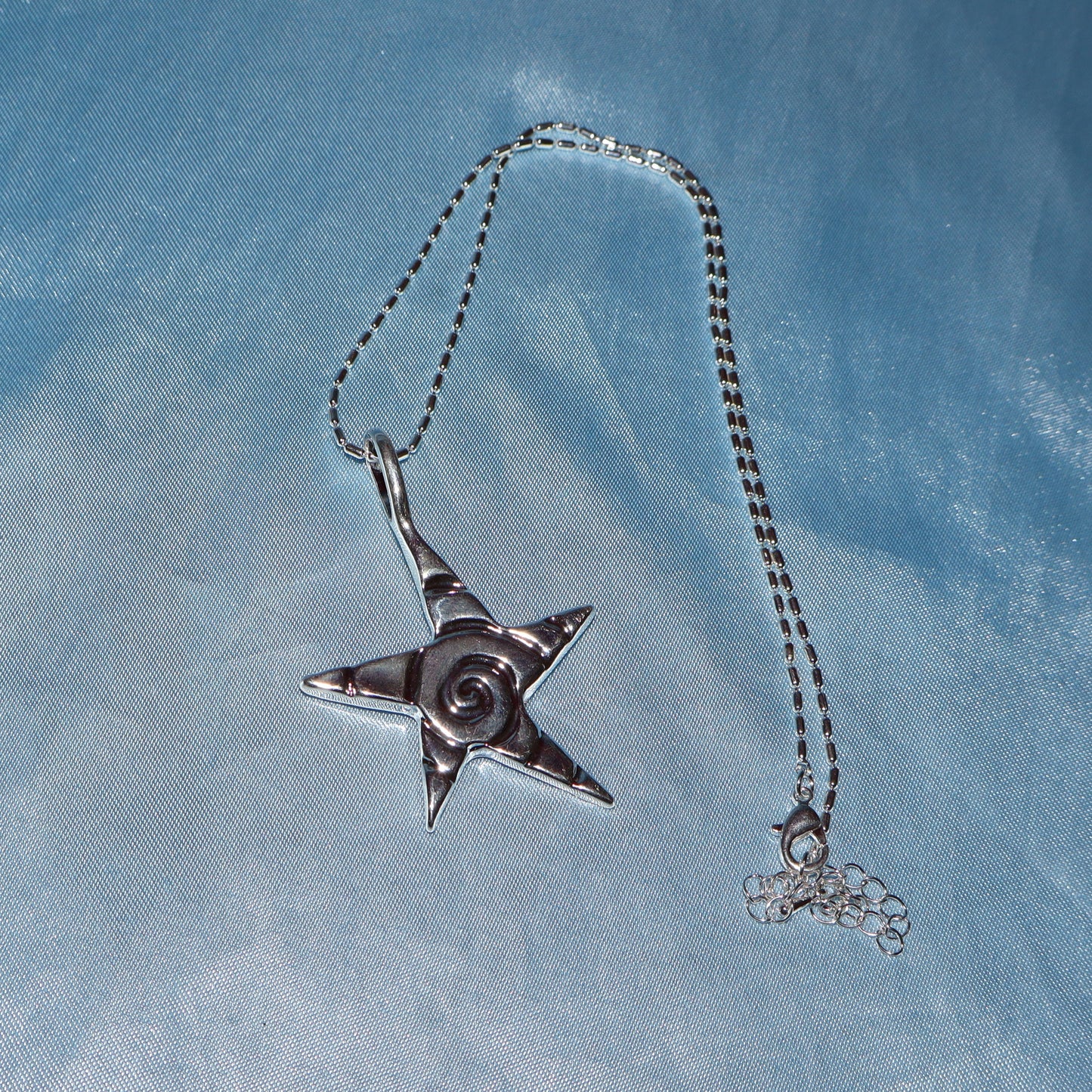 Star pendant, with a swirl design, silver chain necklace.