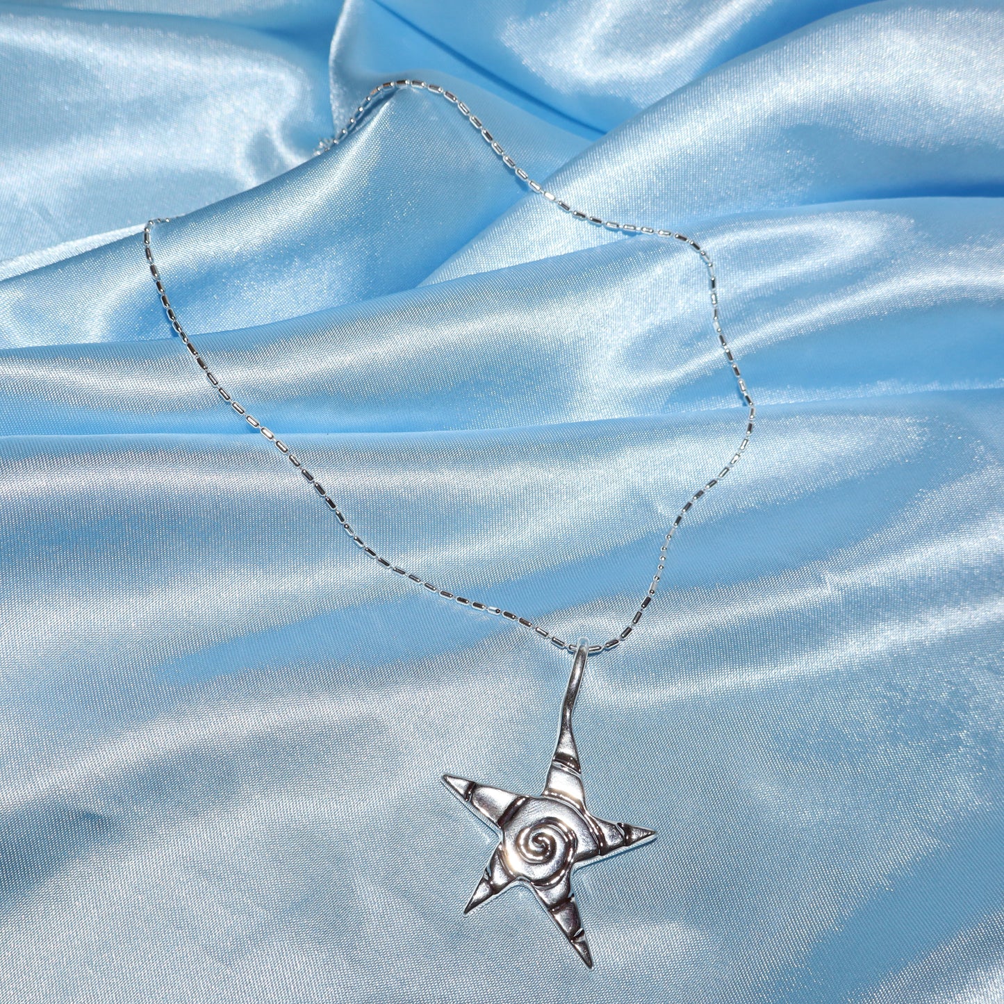 Star pendant, with a swirl design, silver chain necklace.