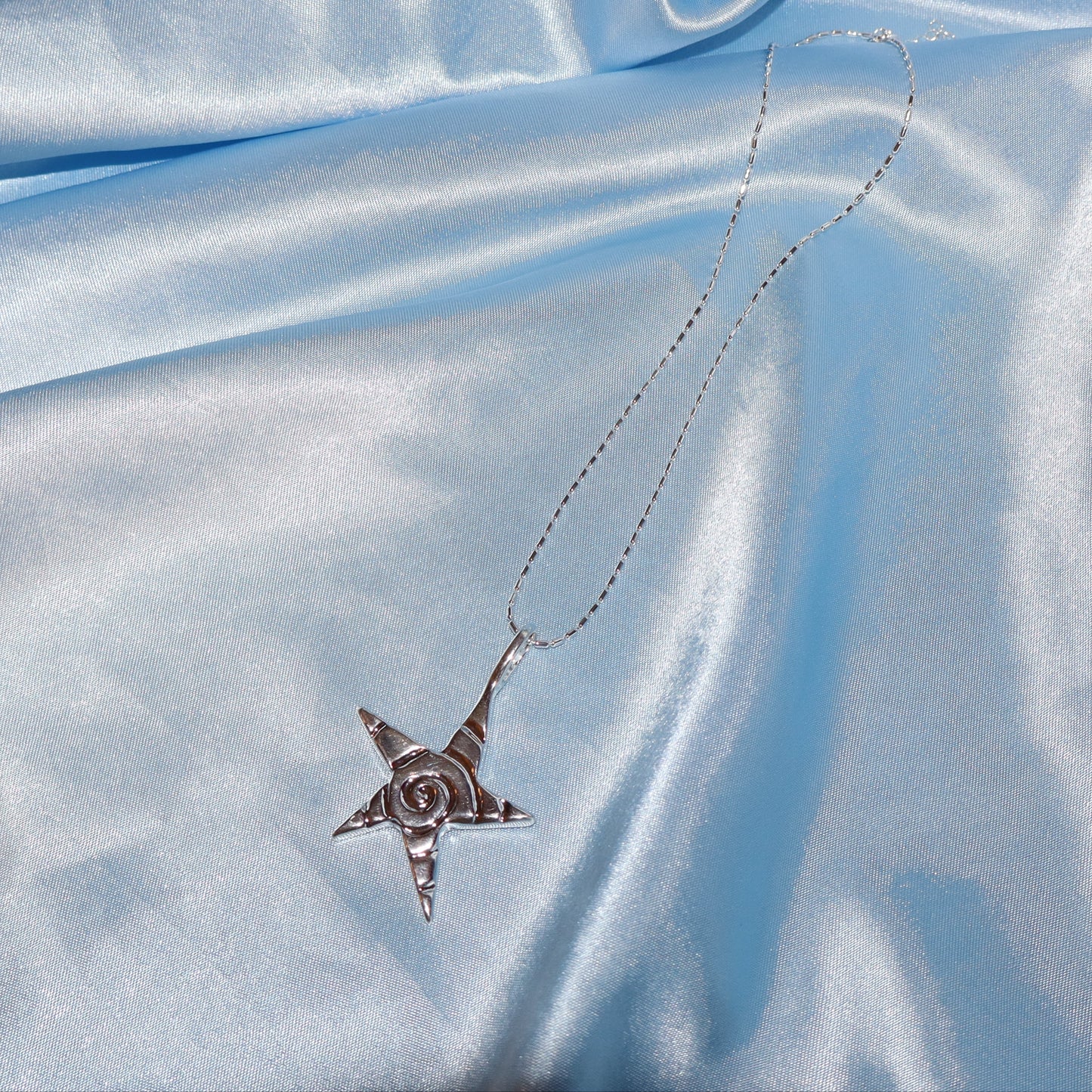 Star pendant, with a swirl design, silver chain necklace.