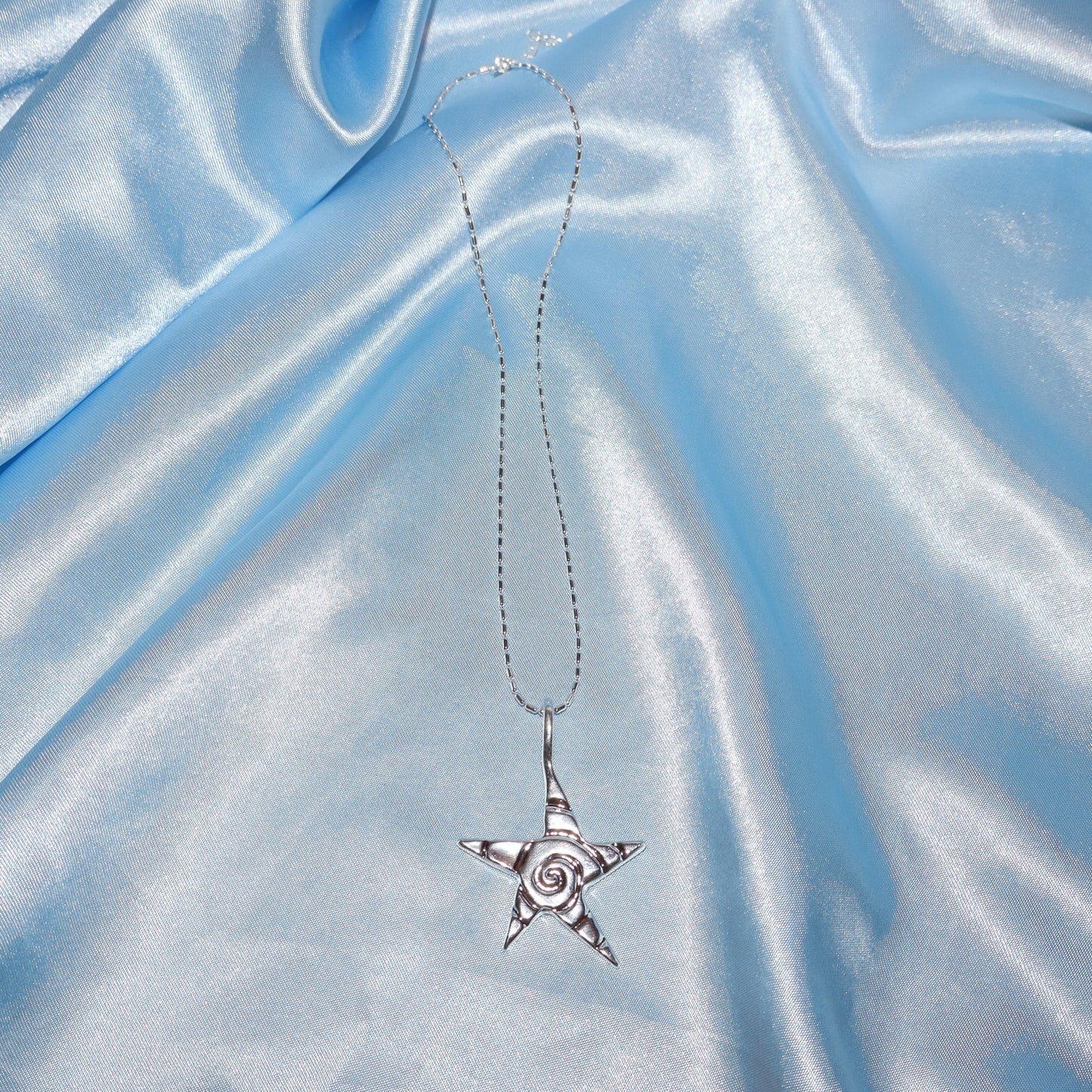 Star pendant, with a swirl design, silver chain necklace.